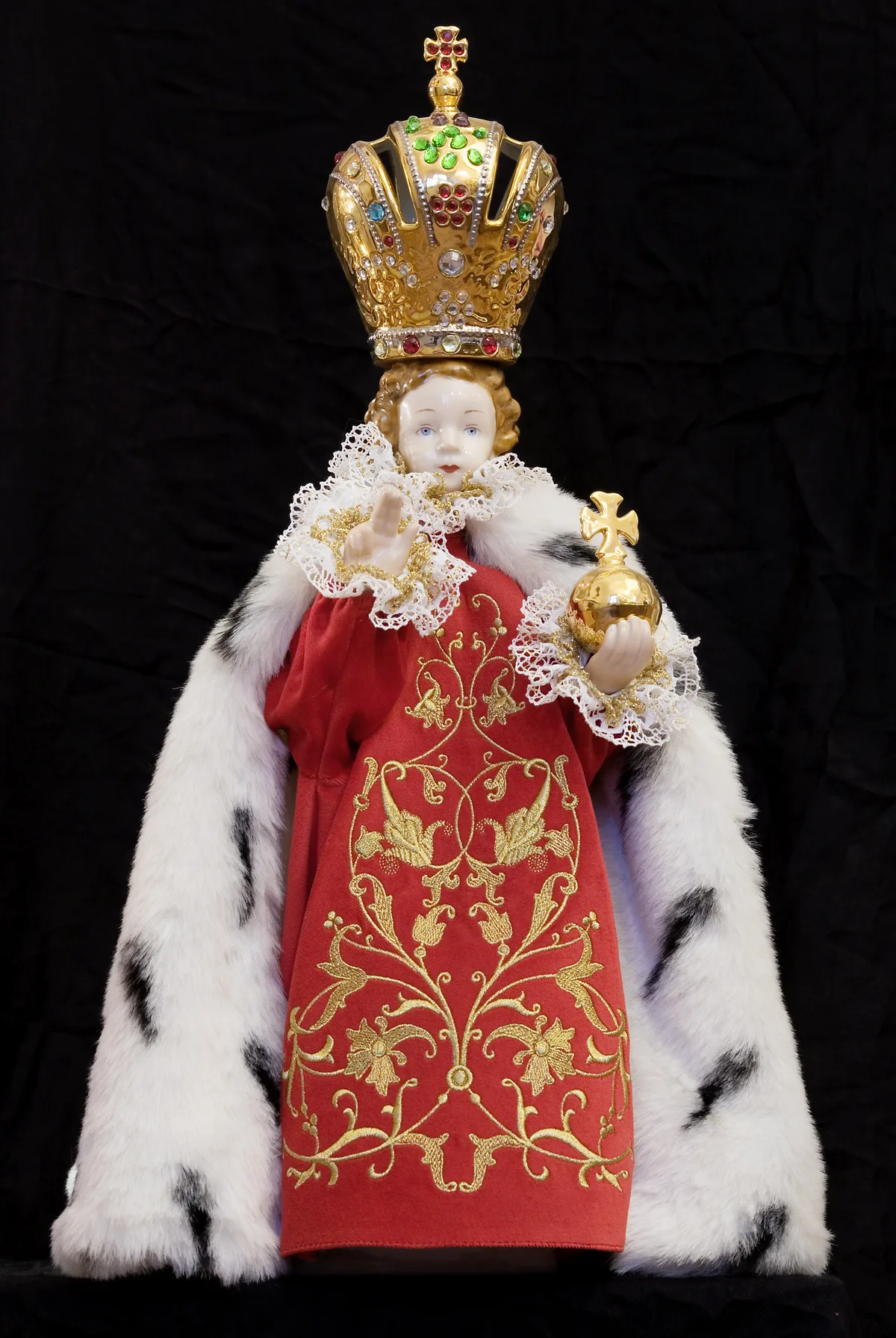 Front view of the Infant of Prague statue in a red and gold robe with an ermine cape and golden crown