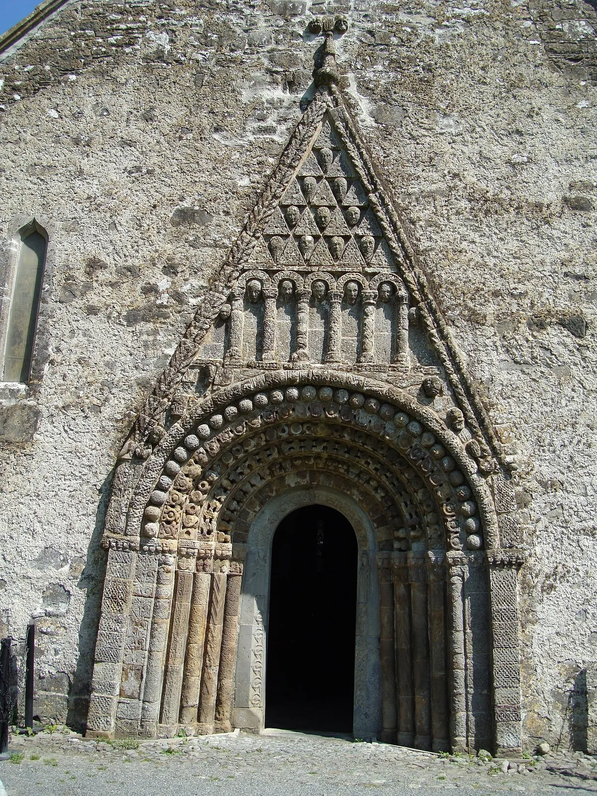The full west doorway of Clonfert Cathedral, a tall Romanesque arch under a triangular pediment filled with carved human heads