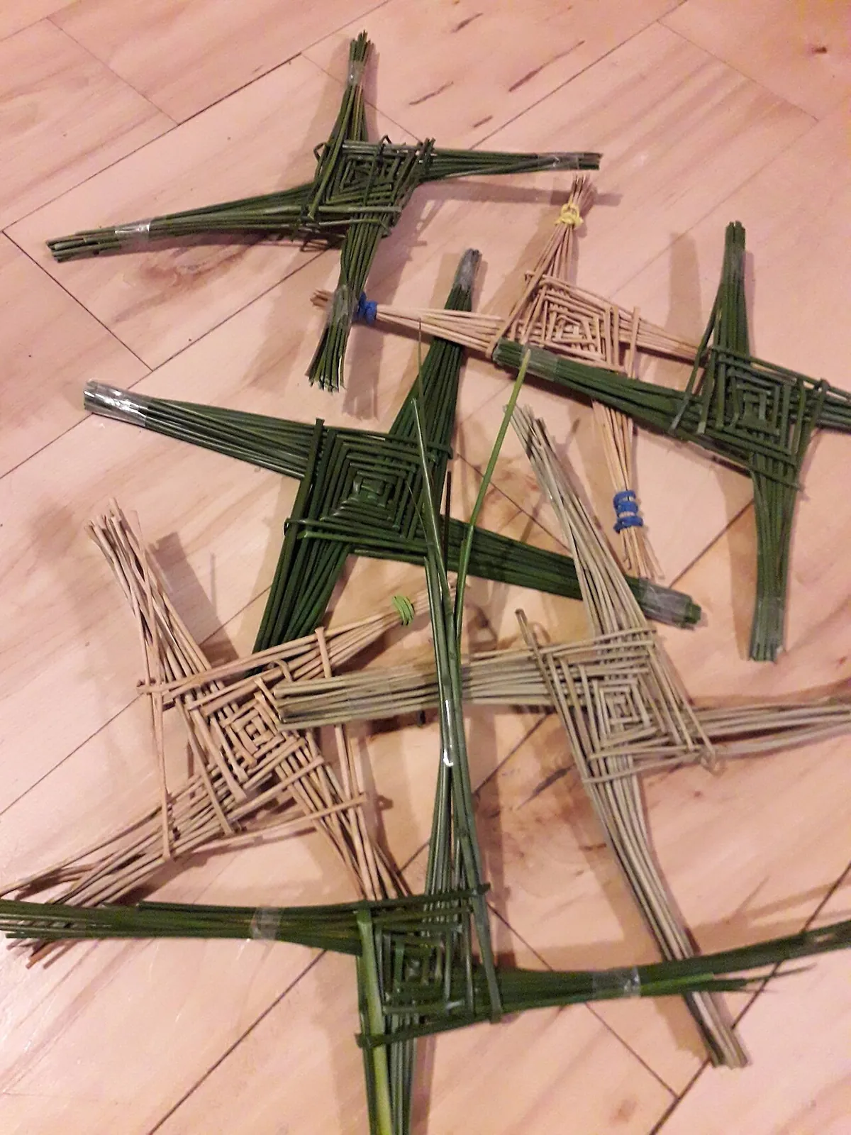 Several Saint Brigid's crosses woven from rushes, the fresh green ones beside older dried examples turned pale gold