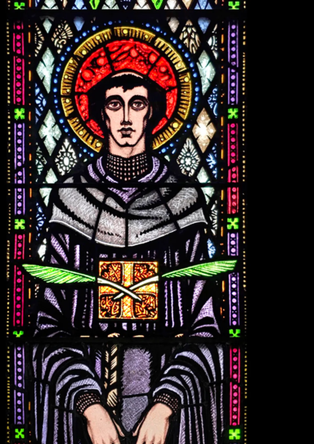 Harry Clarke's Saint Colmcille in stained glass, a young tonsured monk in a dark habit holding a jewelled book against his chest
