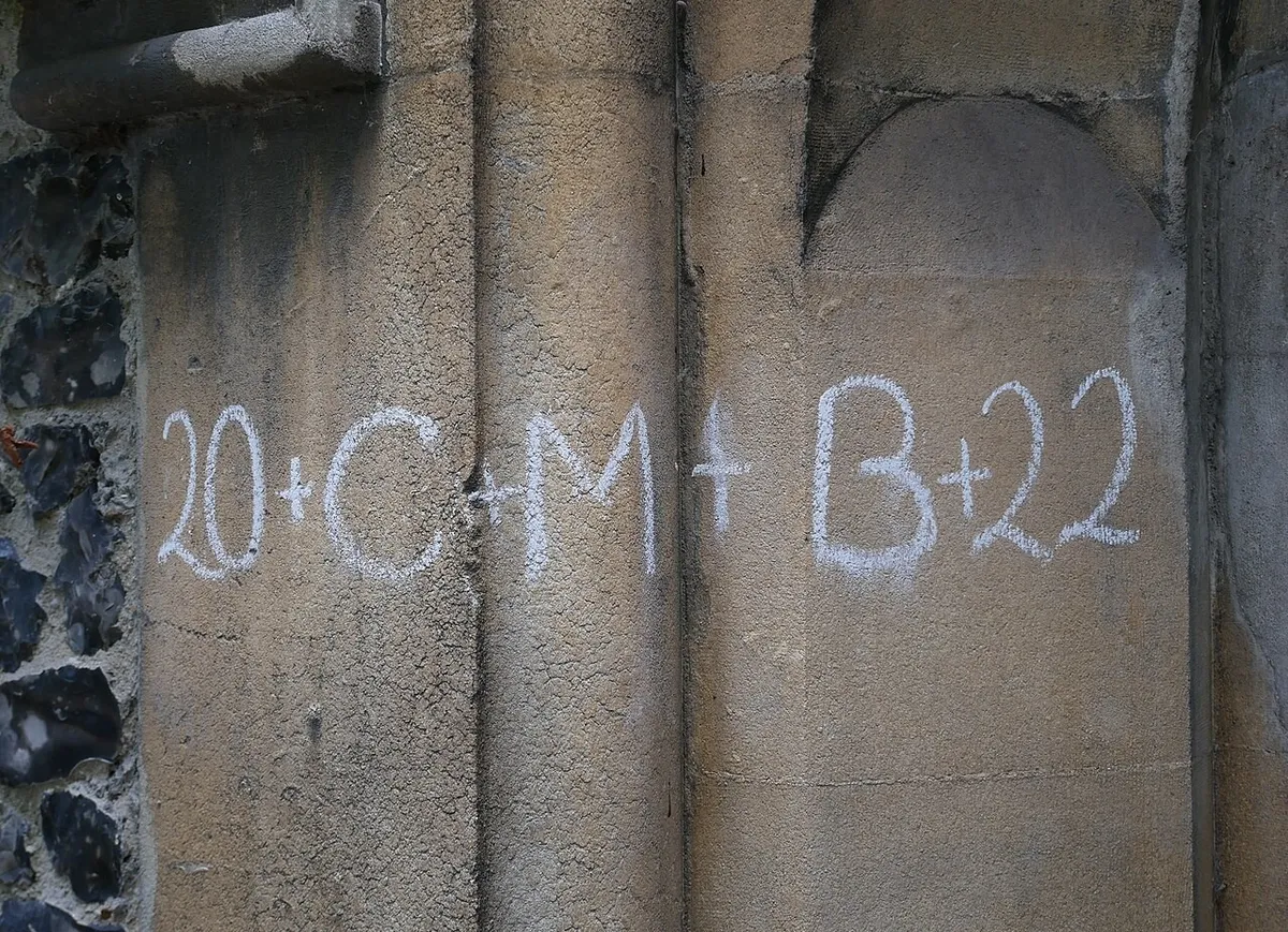 The inscription 20 + C + M + B + 22 written in white chalk on the stone of a church doorway
